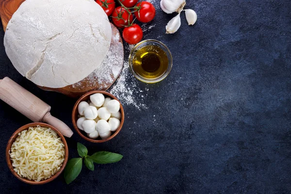 Pizza margherita ingridients çiğ hamur kiraz domates fesleğen zeytinyağı mozzarella peyniri karanlık taş mutfak masasında 