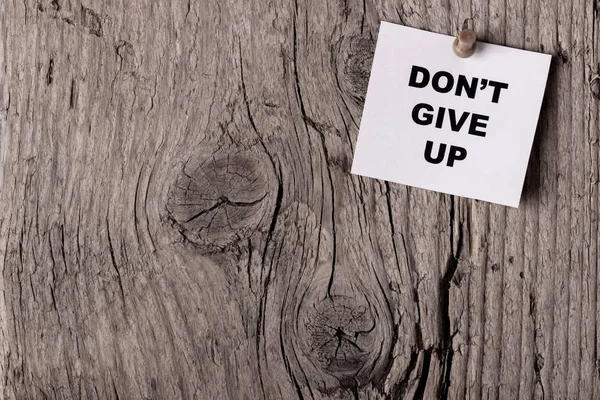 A word Don't give up written on paper pinned to the wooden board