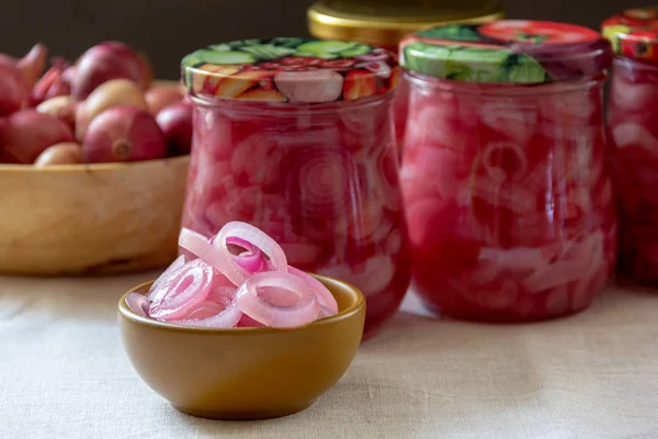 Cup with pickled onions on the background of glass jars