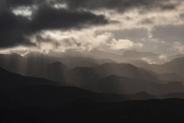 Low clouds, storm clouds with sun rays penetrating, mountainous landscape, dramatic lighting and cloudy atmosphere in Agimes, Gran Canaria, Canary Islands, Spain, Europe