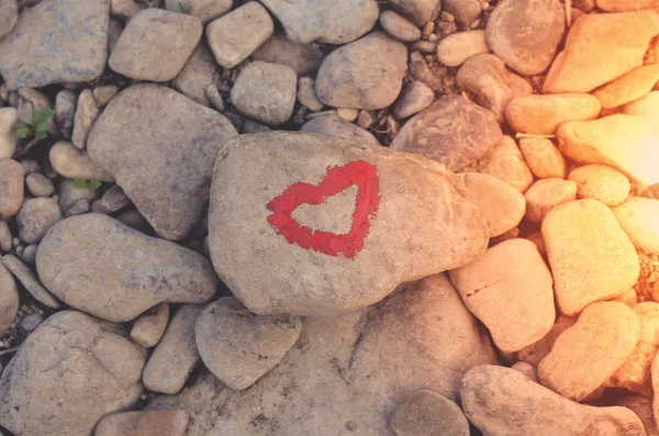Pink heart painted with lipstick on piece of stone on background of many small stones