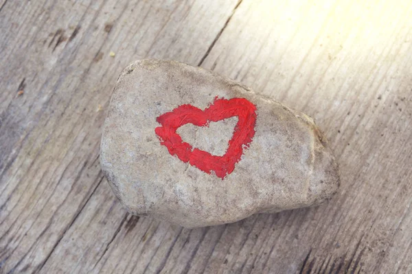 Pink heart painted with lipstick on piece of stone on background of wooden board