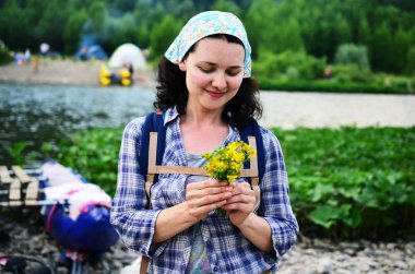 Seyahat kız nehir arka plan üzerinde doğadan alınan sarı çiçekler kokuyor