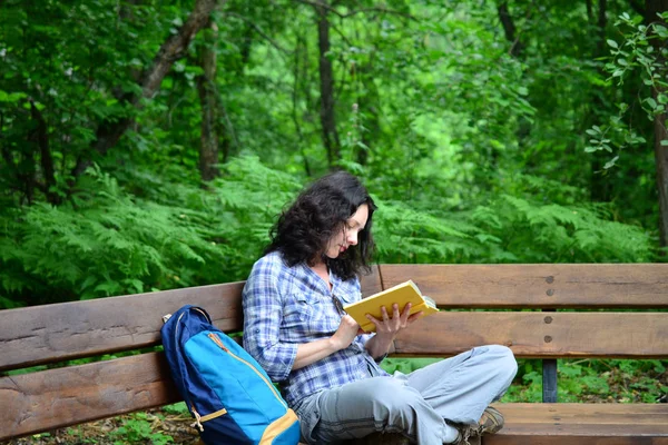 Traveling woman reading book and relaxing at park. Concept of freelance work and study during vacation