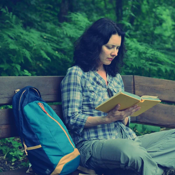 Traveling woman reading book and relaxing at park. Concept of freelance work and study during vacation