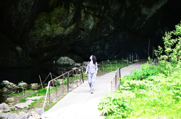 Traveling woman walking on bridge in park near cave