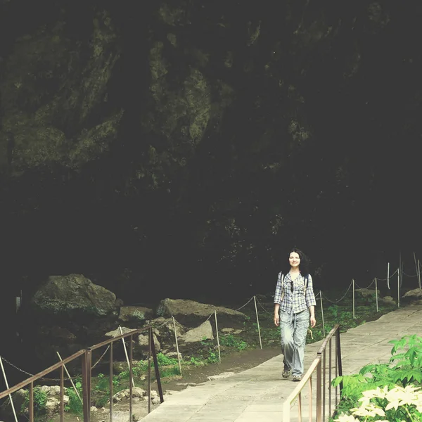 Traveling woman walking on bridge in park near cave