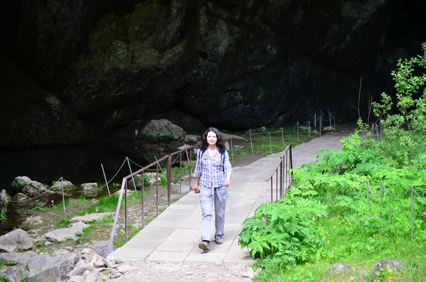 Traveling woman walking on bridge in park near cave