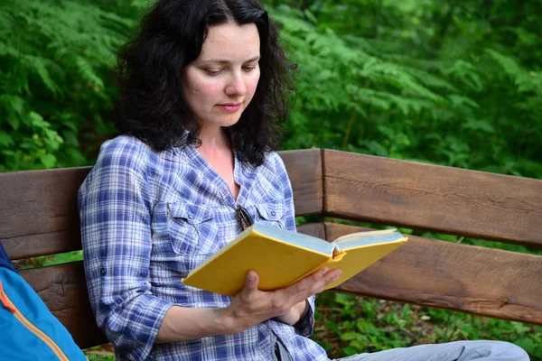 Traveling woman reading book and relaxing at park. Concept of freelance work and study during vacation