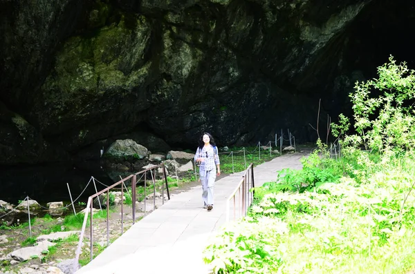 Traveling woman walking on bridge in park near cave