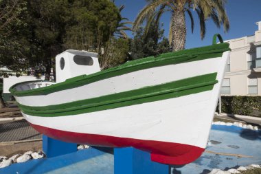 La Isla Plana/ Endülüs, İspanya : 27 Ocak 2019: palmiye ağaçlarıyla dolu bir bahçede mavi bloklar üzerinde yeşil, kırmızı ve beyaz ahşap balıkçı teknesi.