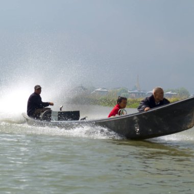 Inle gölü, Shan State, Myanmar (Burma) - 24 Ocak 2016 : Bambu teknesi gölde sabahın sisinde iki adam ve uçaktaki sürücüyle birlikte sprey kusuyor. Gölün kıyısında, köy sisin içinde..