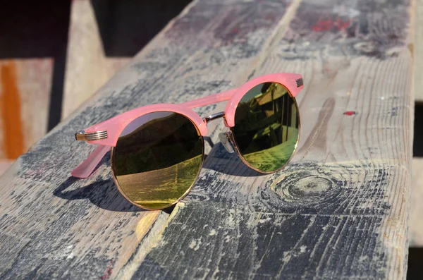 Pink napszemüveg a nap ellen egy fából készült háttér közelében — Stock Fotó