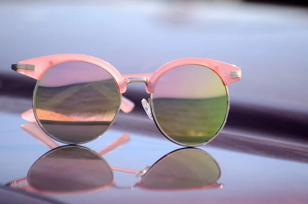 Lunettes de soleil roses contre le soleil sur le capot d'une voiture — Photo