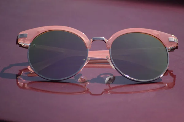 Rosa Sonnenbrille gegen die Sonne auf der Motorhaube eines Autos — Stockfoto