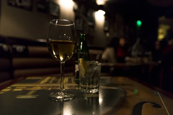 A glass of white wine and a soda on a table in a bar