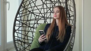 Güzel genç kadın telefonla bir kolye sandalyede oturur ve müzik dinliyor