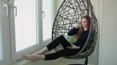 Güzel genç kadın telefonla bir kolye sandalyede oturur ve müzik dinliyor