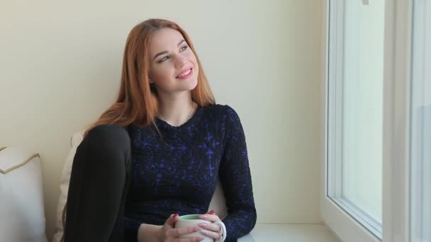 Güzel genç kadın oturur evde pencere ve bir şey hakkında hayal ederken pencereden görünüyor — Stok video