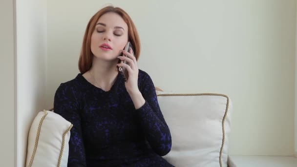 Mulher bonita lê um livro e fala pelo telefone enquanto se senta no parapeito da janela em casa — Vídeo de Stock