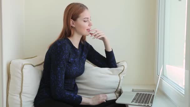 Mulher bonita se comunica em redes sociais em um laptop enquanto se senta no parapeito da janela em casa — Vídeo de Stock