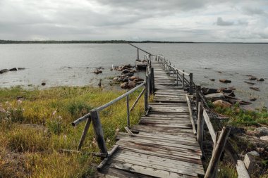 Eski ahşap yürüyüş yolları denize. Bulutlu gökyüzü.