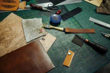 Leatherworking araçları. Riveter, tığ, cetvel, pense, püsküllü, kalem, deri parçaları, perçin ve bağlantı elemanları masaya vardır. Fotoğrafı kapatın.