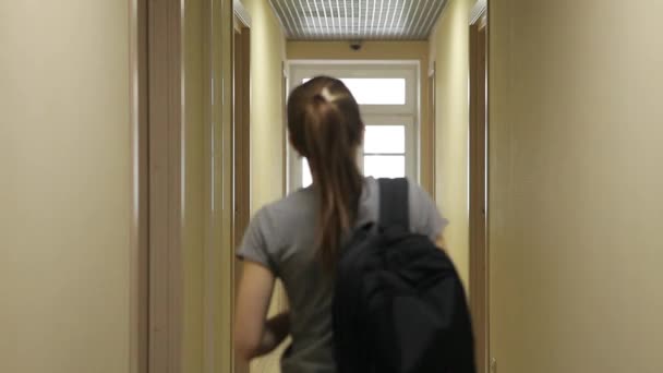 Une jeune fille avec un sac à dos marche le long du couloir de l'hôtel et entre dans sa chambre . — Video