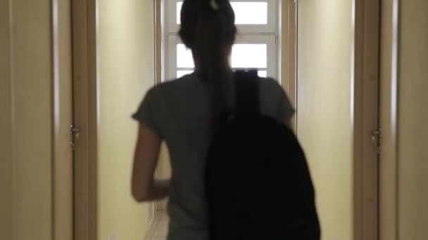 A young girl with a backpack walks along the corridor of the hotel and enters her room. — Stock Video