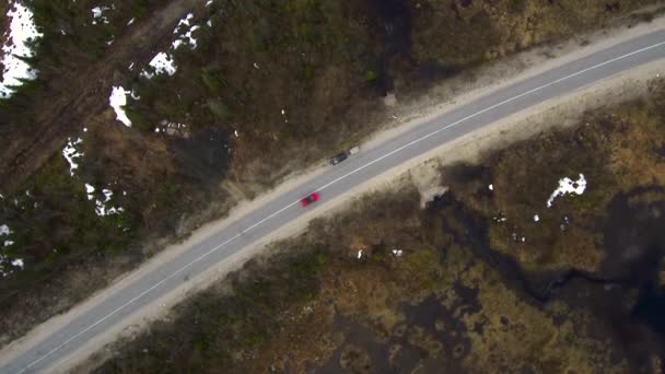 Vista aerea della foresta di abete rosso e palude in primavera. Paesaggio Taiga in una giornata nuvolosa. L'arco del drone sulla strada forestale. Auto rossa guida lungo la strada . — Video Stock