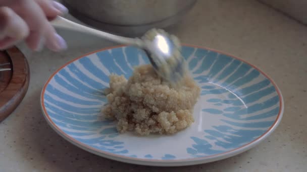 Die weibliche Hand legt Quinoa-Brei auf einen Teller. Nahaufnahme. — Stockvideo