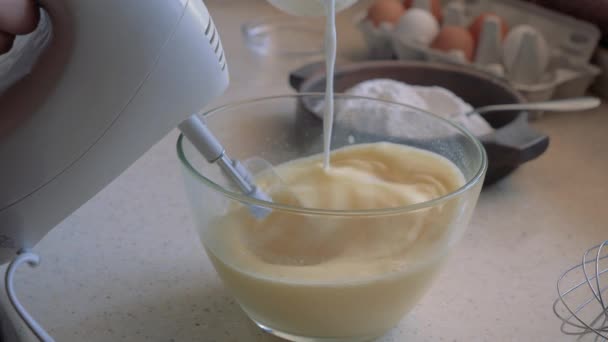 女性の手はボウルにミキサーの卵を混ぜます。ボウルに牛乳を加える. — ストック動画