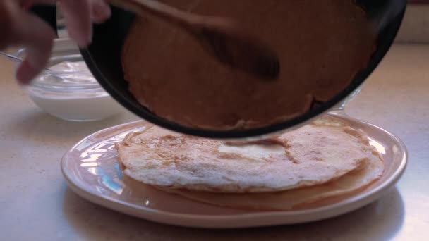 Spread pancake from the pan in a plate. Stack of hot classic Russian thin pancakes. Rustic style. Traditional for the Russian pancake week - Maslenitsa. Sour cream, butter and eggs in the background. — Stock Video
