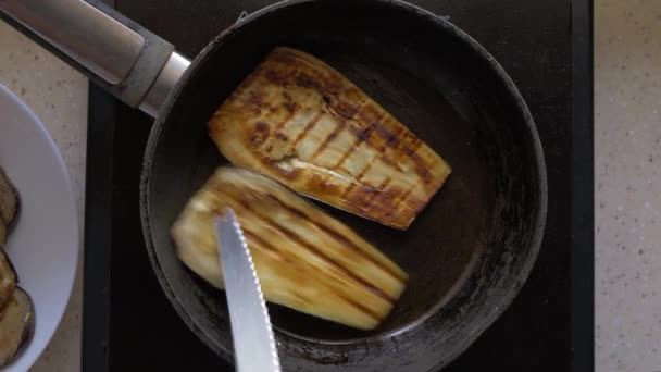 Auberginen, in Scheiben geschnittene Scheiben werden in einer Pfanne in Butter angebraten. Frauenhände mit einem Messer drehen sie um. Nahaufnahme, Draufsicht. — Stockvideo