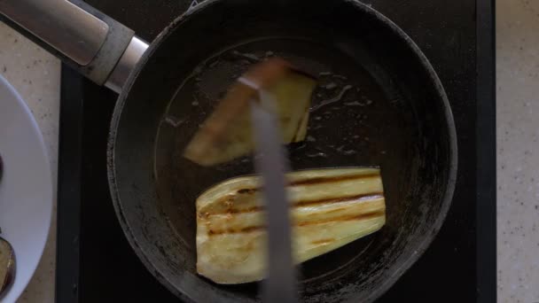 Auberginen, in Scheiben geschnittene Scheiben werden in einer Pfanne in Butter angebraten. Frauenhände mit einem Messer drehen sie um. Nahaufnahme, Draufsicht. — Stockvideo