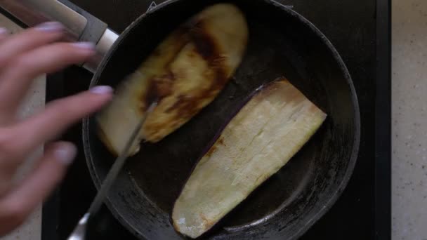 Aubergine, tranches tranchées sont frites dans le beurre dans une poêle. Les mains féminines avec un couteau les retournent. Gros plan, vue de dessus . — Video