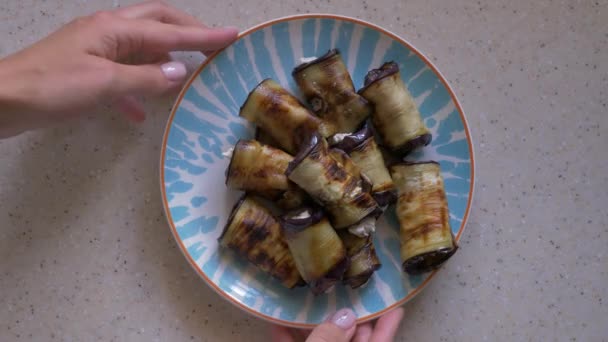 A woman puts on the table a plate of fried eggplant with filling. Close-up, top view. — Stock Video