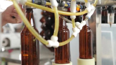 Birbira fabrikasında bir makine bir şişe bira doldurur. Arka plandaki bir makine operatörü işlemi denetler. Close.