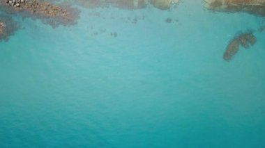 Deniz sahilinin havadan görünümü. Dalgalar taş bir plajın yakınına sıçrayan. Masmavi berrak su.