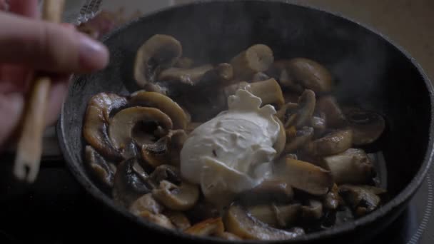 Os cogumelos fritam-se em uma panela, acrescentam a nata e a mistura . — Vídeo de Stock