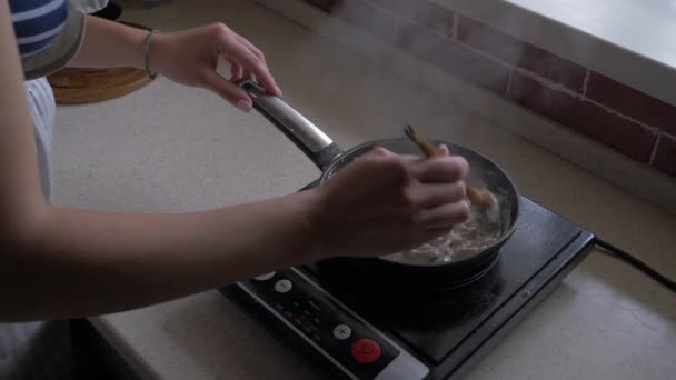 Vrouw roert paddestoelen in een koekenpan met uien en room. — Stockvideo