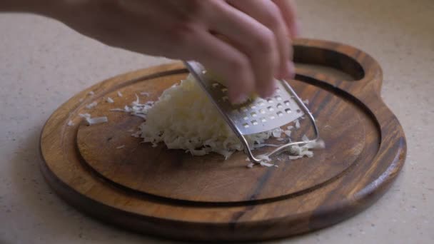 A mão feminina esfrega o queijo em uma tábua de corte . — Vídeo de Stock