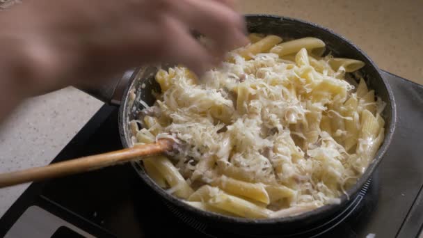 En kvinnlig hand lägger riven ost till pasta, som är stekt i en stekpanna. — Stockvideo