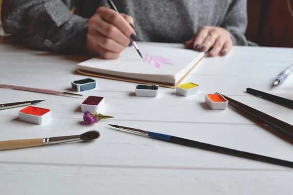 Uma Mulher Pinta Num Caderno Esboços Ferramentas Para Pintar Mesa — Fotografia de Stock