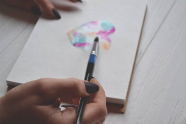 Kadın boyalar bir eskiz defteri içinde. Beyaz ahşap masa üzerinde boyama için araçlar. Ressam iş.
