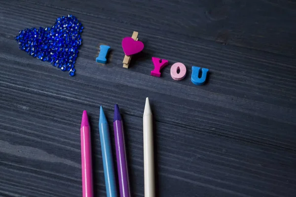 Colorful pencils, love heart and letters on a blue wooden background.