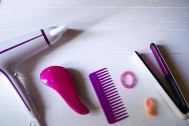 Saç bakım aletleri. Güzellik Salonu. Saç bakım araçları Beyaz ahşap zemin üzerinde. Saç kurutma makinesi, saç maşası, tarak ve parlak sarmal scrunchies.