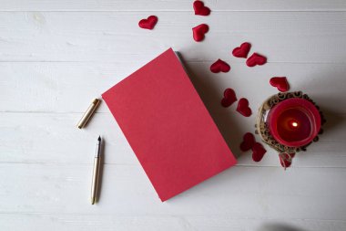 Bir masa üzerine kırmızı defter, mum ve sevgi kalpleri.
