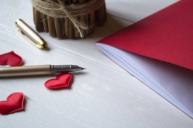 Bir masa üzerine kırmızı defter, mum ve sevgi kalpleri.
