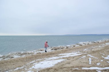 Genç kadın kış sahilde yürüyor.